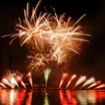 Golden fireworks reflected in water during a night festival