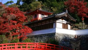 Red maple leaves beside a Japanese temple and vermilion bridge